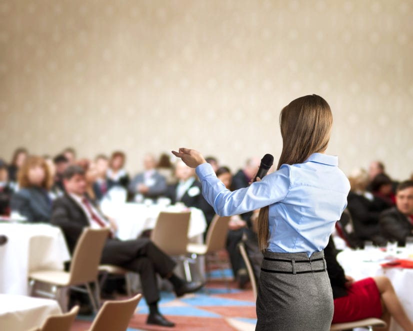 Young woman speaks to tabled audience at business conference