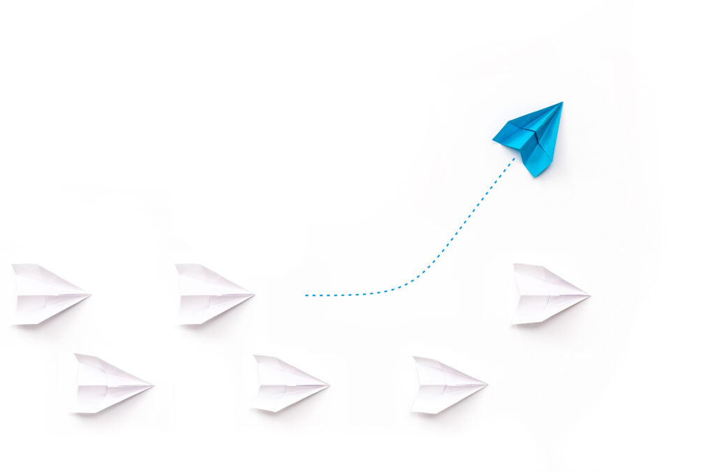 A group of paper airplanes, one plane is flying in the other direction, different way.