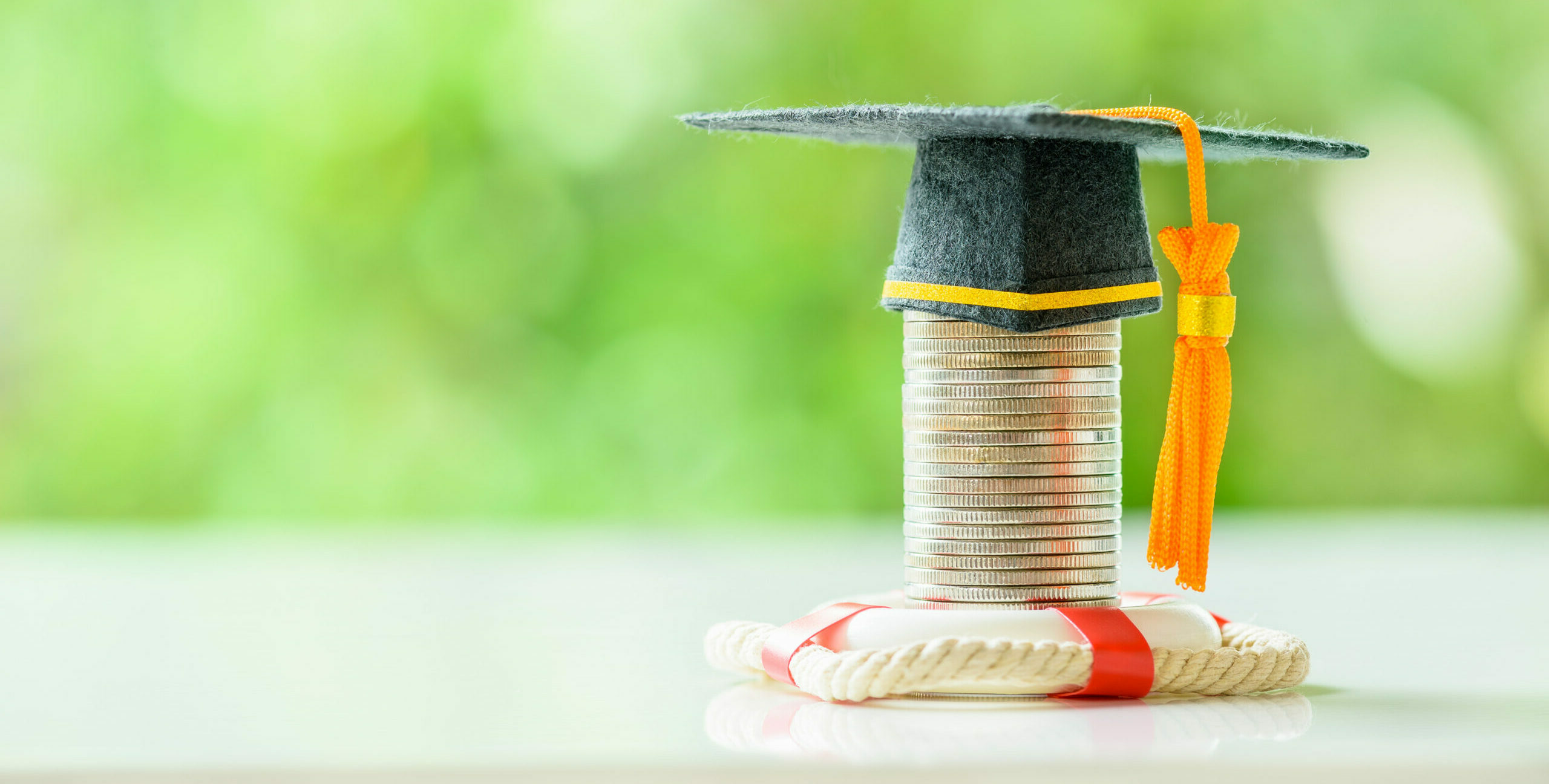 Tuition protection service, financial concept: Black graduation cap placed on top of a coin stack with a red lifebuoy on a table.