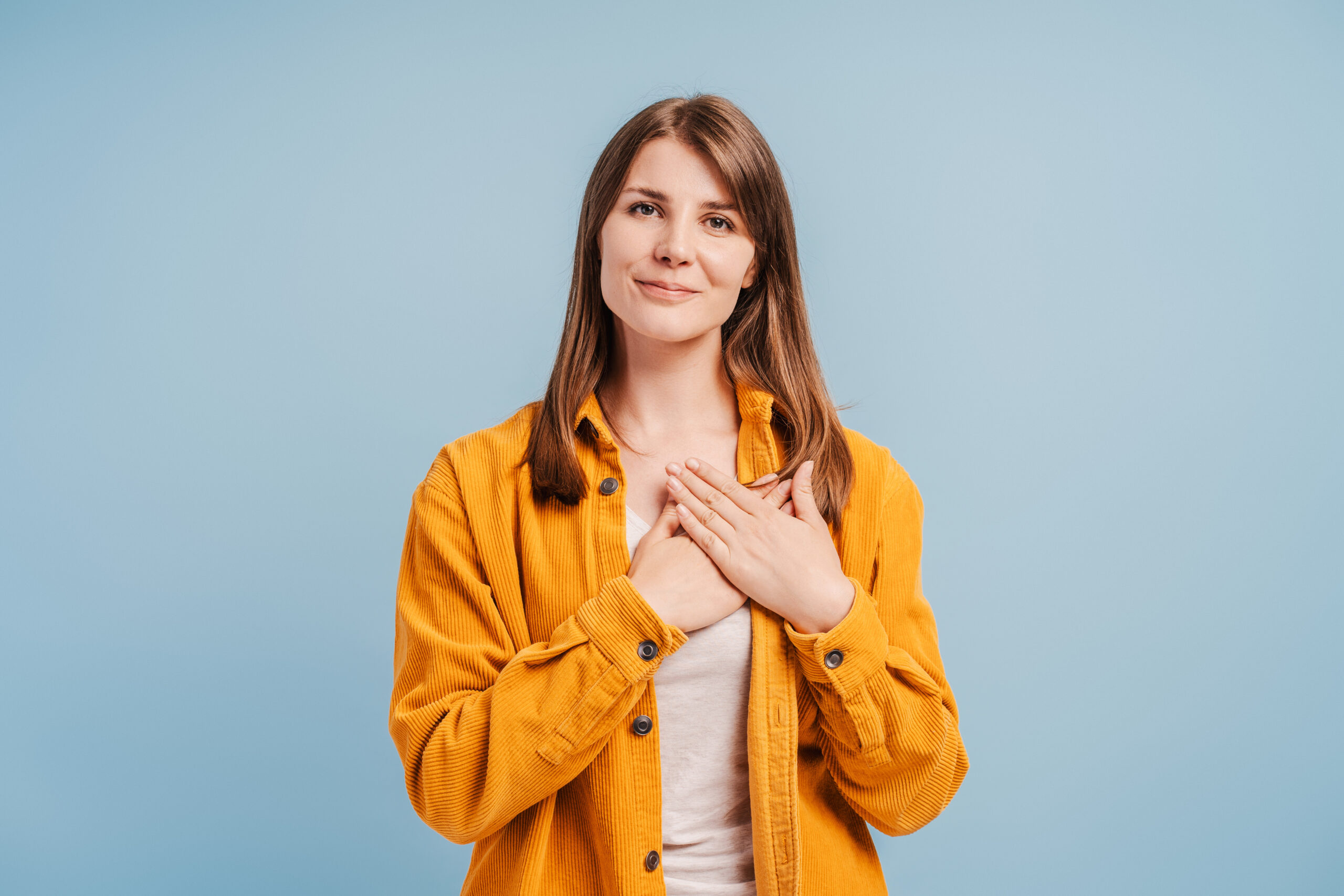 Portrait of young woman holding hands over heart, gesturing with appreciation looking at camera isolated on blue background.