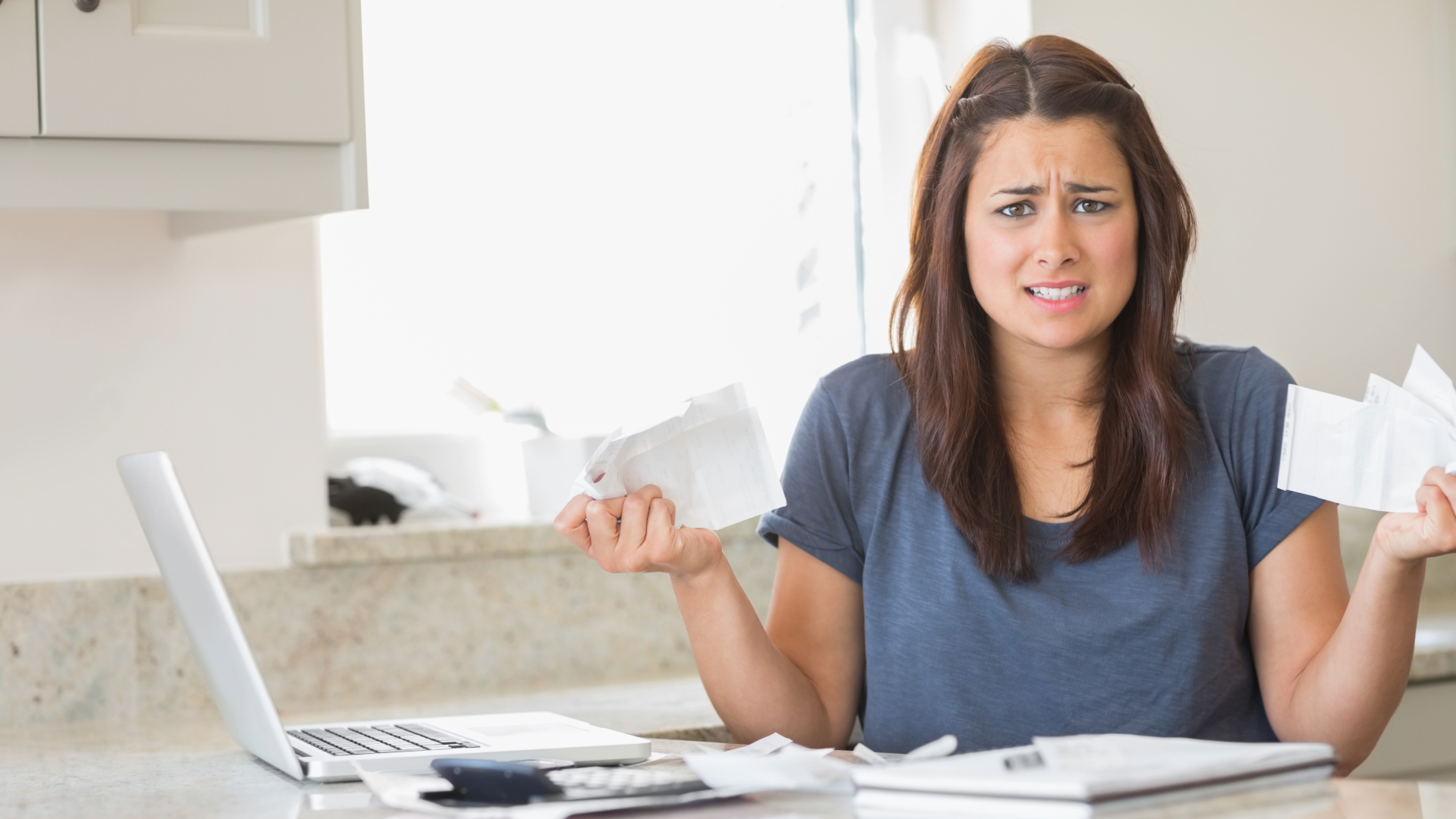 Woman looking troubled while holding bills in the kitchen.