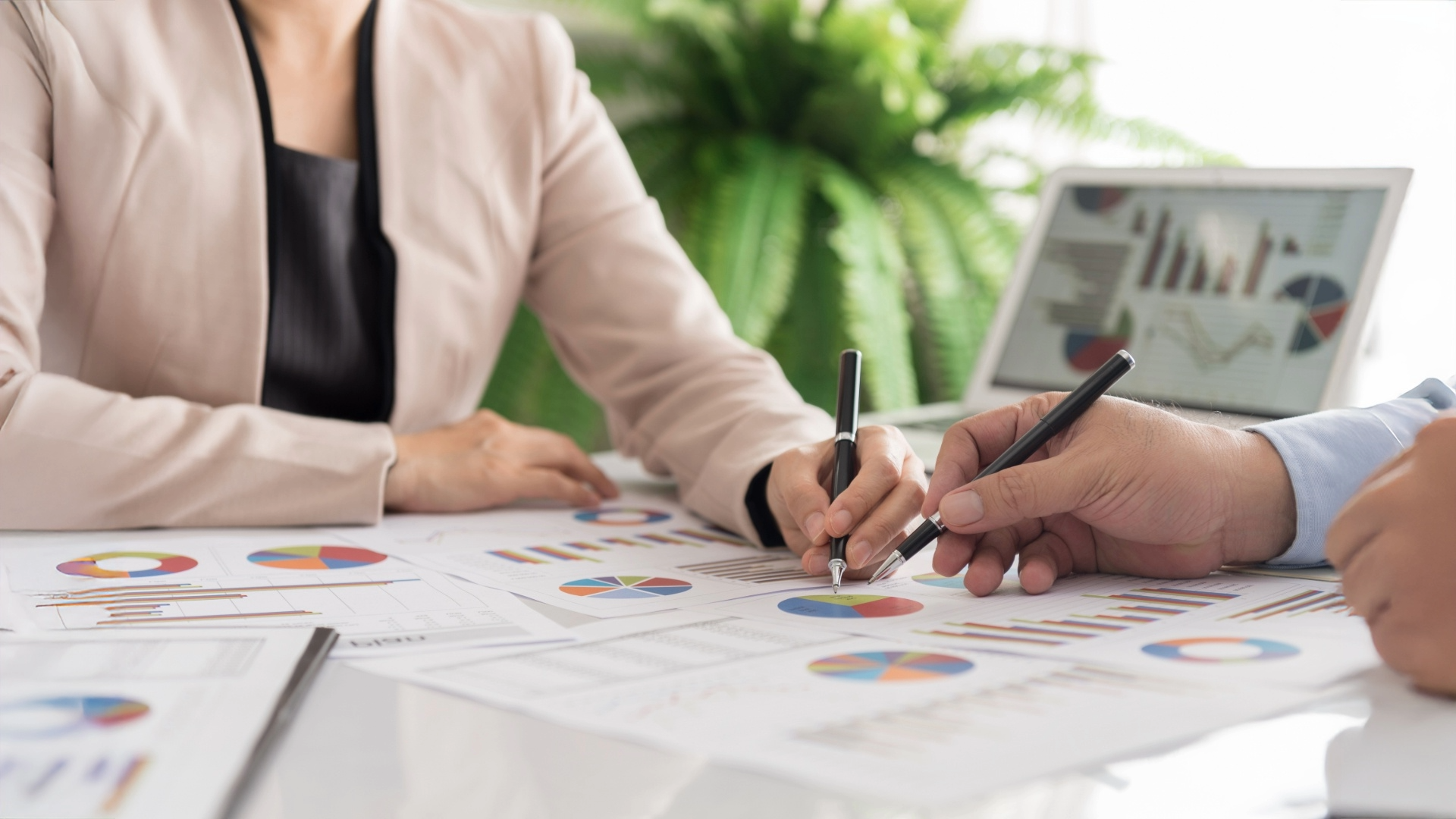 Two business people meeting at a table. Only their hands with pens are showing as they are looking at financial documents.