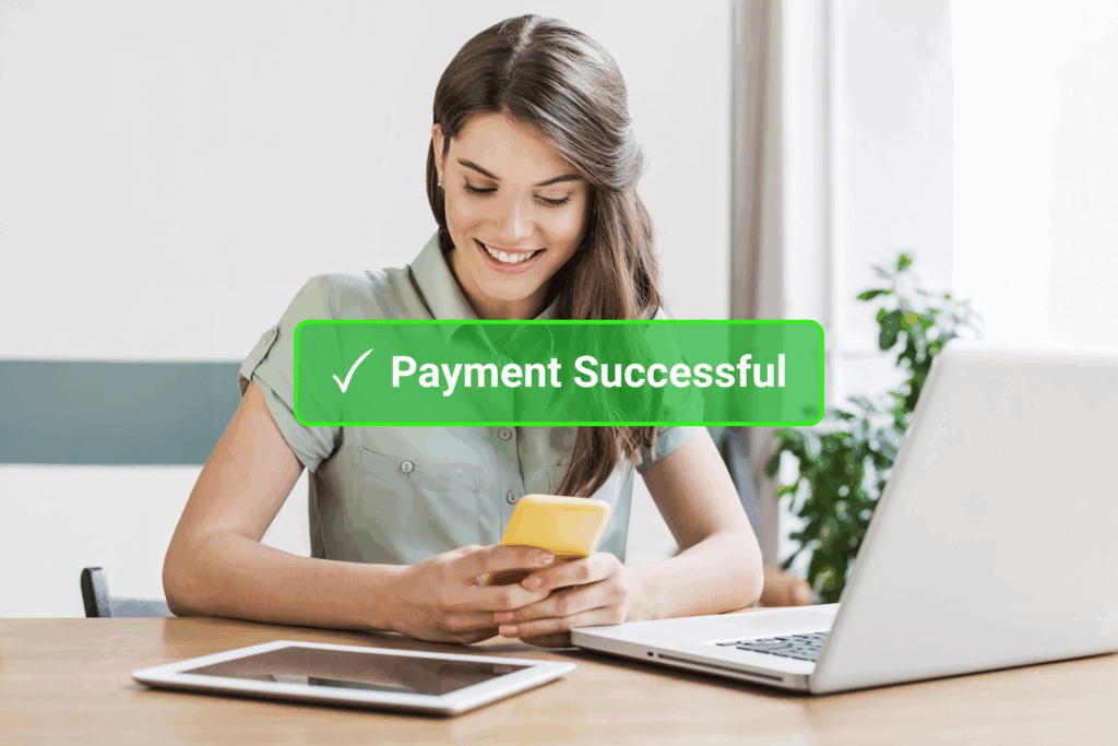 Young smiling woman with mobile phone in hand, laptop and tablet on table. "Payment Successful" in green bar displayed centered over image.