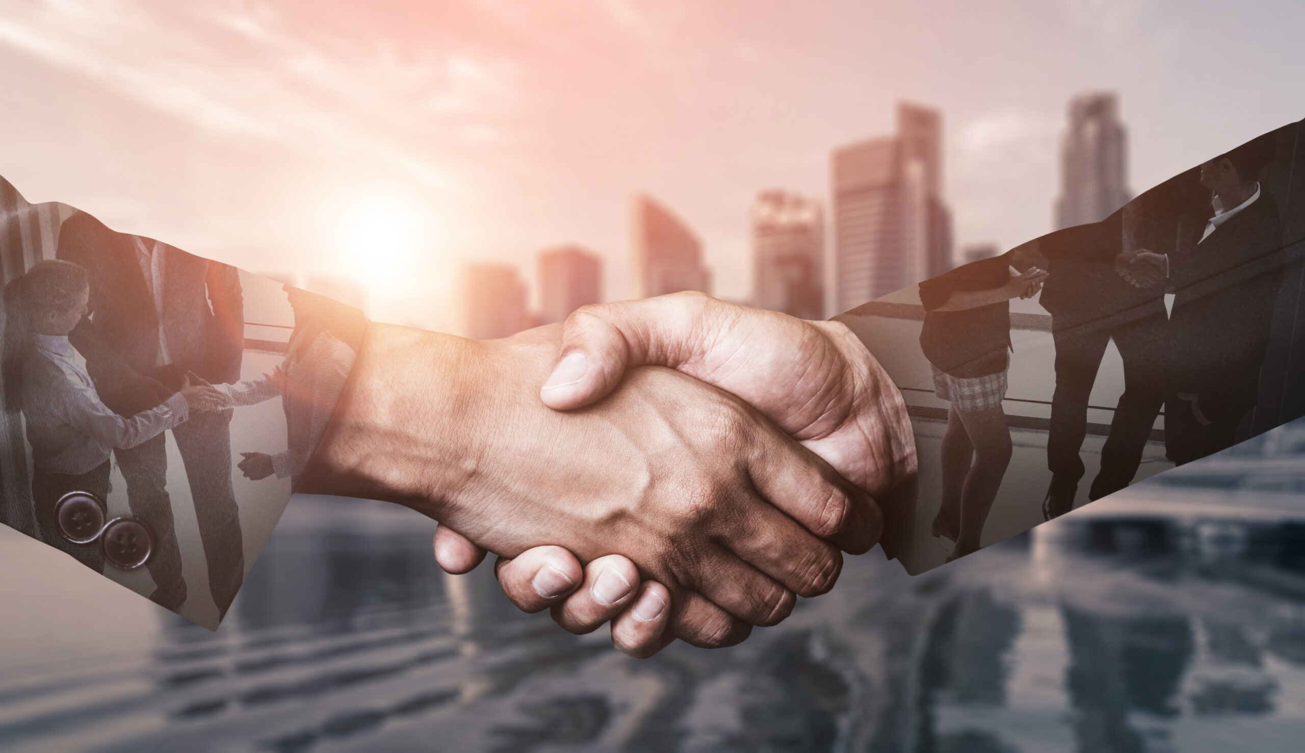 Double exposure image of business people handshake on city office building in background showing partnership success of business deal.