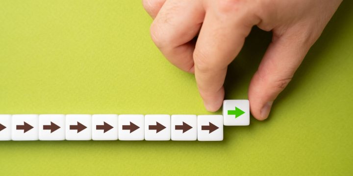 A hand makes a path out of blocks with arrows. The concept of moving forward and continuing progress. Strategic planning, forward momentum, and the continual pursuit of growth and improvement.